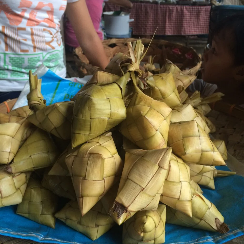 A close-up view of a pile of Cebuano puso or hanging rice—cooked rice wrapped in woven coconut leaves—on display at a local market.